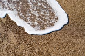 Close-up of the white wave, on the beautiful, sandy beach