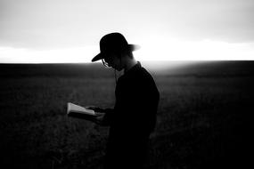 Guy reads a book on the field in black and white background