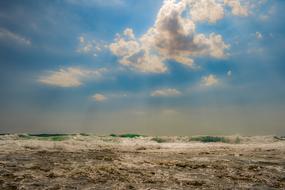 Beautiful and colorful seascape with the waves, under the blue sky with clouds, in light