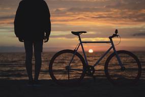 Silhouette of a person, near the bicycle on the beautiful shore of the ocean, at colorful sunrise on horizon