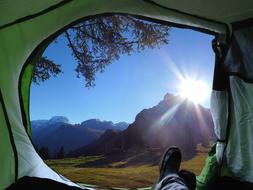 View of the colorful and beautiful mountains in sunlight, from the tent with person, among the plants