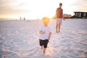 Child with father, walking on the sandy beach in sunlight among the clouds