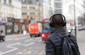 Guy in headphones, and with backpack on the street with vehicles and buildings