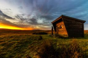 a man stands near a wooden hut during sunset
