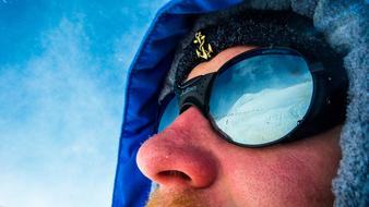 male face in protective glasses with snowy mountains reflection