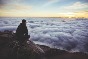 man sits on mountain summit over Clouds