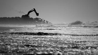 Black and white landscape with the sea beach with silhouette of the excavator, near the water in light