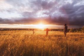 people stand in the meadow during sunset