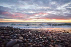 Close-up of the beautiful beach with pebbles, near the water with waves, under the sky with colorful clouds