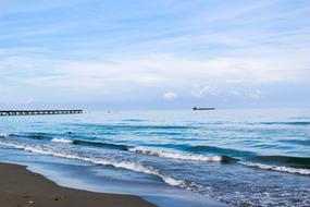 Beautiful sandy beach of the ocean, with colorful waves, under the blue sky with white clouds