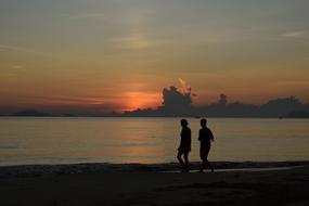 silhouettes of two people on the sea coast at sunset