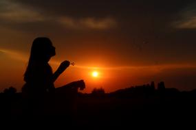 Silhouette of the girl blowing bubbles on the landscape, at colorful and beautiful sunset