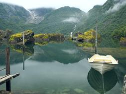 Beautiful landscape of the water with colorful Bondhusvatnet and boat, among the colorful mountains with plants in fog, in Norway
