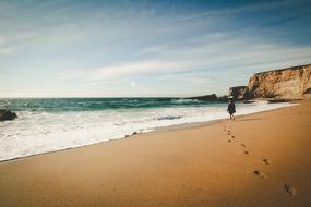 Beautiful landscape of the sandy beach of the ocean with person and footprints, under the blue sky with clouds