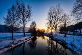 winter trees along a calm river in val de travers, Neuchatel in Switzerland