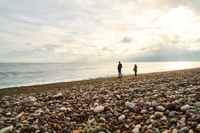 People on the beautiful beach with colorful stones, near the water with waves