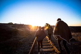 people walking on railway rails in the background of sunset