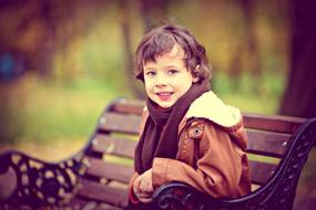 happy child boy sits on Bench In Park at Autumn