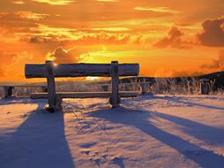 Beautiful, snowy landscape with the bench on the mountain, at colorful and beautiful sunset with clouds