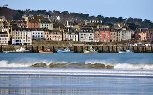 Beautiful and colorful houses and boats on the coast of the sea with waves, in Douarnenez, Brittany, France