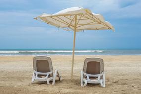 two sun loungers under an umbrella on the beach on a cloudy day