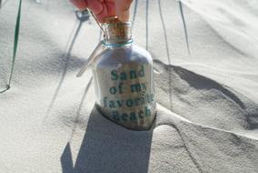 Person holding bottle with favorite beach sand, in the sand in sunlight