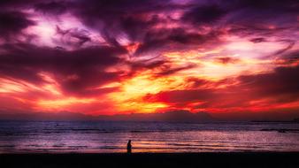 Silhouette of the person, on the beautiful beach with waves, at colorful and beautiful sunset, among the clouds