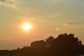 distant view of the silhouette of a house on a hill at sunset