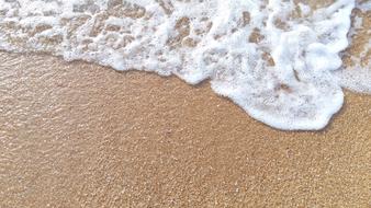 Close-up of the beautiful, shiny wave of the sea, on the sandy beach in sunlight