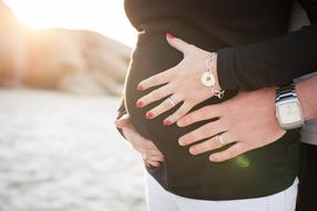 pregnant woman with man on the beach in sunlight
