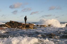 Man doing sea trout fishing on the coast with rocks, in waves, in Bornholm, Denmark