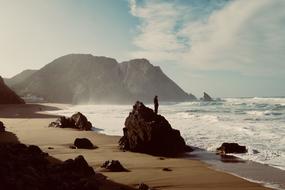 man stands on a rock by the ocean