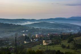 Beautiful landscape with the buildings on the green hills with plants, in fog, at colorful and beautiful sunset