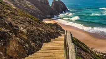 Beautiful landscape of the sandy seashore with wooden stairs and colorful rocks, in sunlight