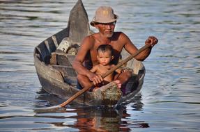 Man in hat, with the child, swimming on the wooden boat, on Tonle Sap in Cambodia