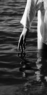 Black and white photo with close-up of the hand of a girl, walking in the water with ripple