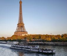 Boat on the beautiful Seine river near the coast with colorful trees and Eiffel Tower, in Paris, France