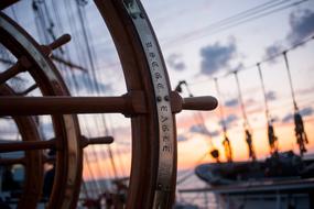 wooden steering wheel of a ship against a blurred sunset background