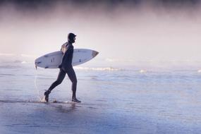 Surfer with surfboard, walking on the water with splashes, near the mist