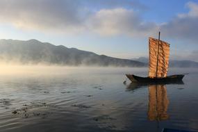 traditional asian sailing boat anchored on water near foggy coast