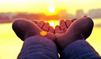 Person holding hands at background with landscape with buildings, at colorful and beautiful sunset