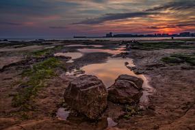Beautiful landscape with the rocks and green grass on the beach of the sea, at beautiful and colorful sunset in clouds