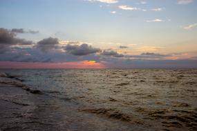Beautiful beach of the sea, with waves, at colorful and beautiful sunset behind the clouds