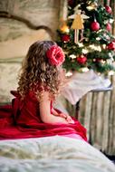 Child Girl sits on bed looking at Christmas tree