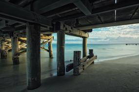 Under view of the pier on the sandy beach, under the blue sky with clouds