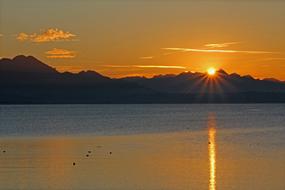 sunset over the silhouettes of the mountains over the water