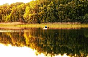 Beautiful lake with the boat with person, near the colorful and beautiful trees in sunlight, with reflections