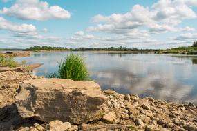 Beautiful coast of the river with rocks and green plants, under the blue sky with clouds