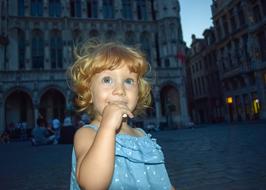 Portrait of the cute, blonde girl child with blue lights, on the square, among the buildings