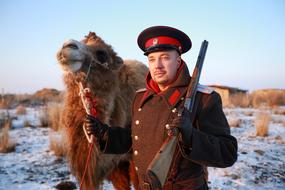 military man with a camel on a field in winter